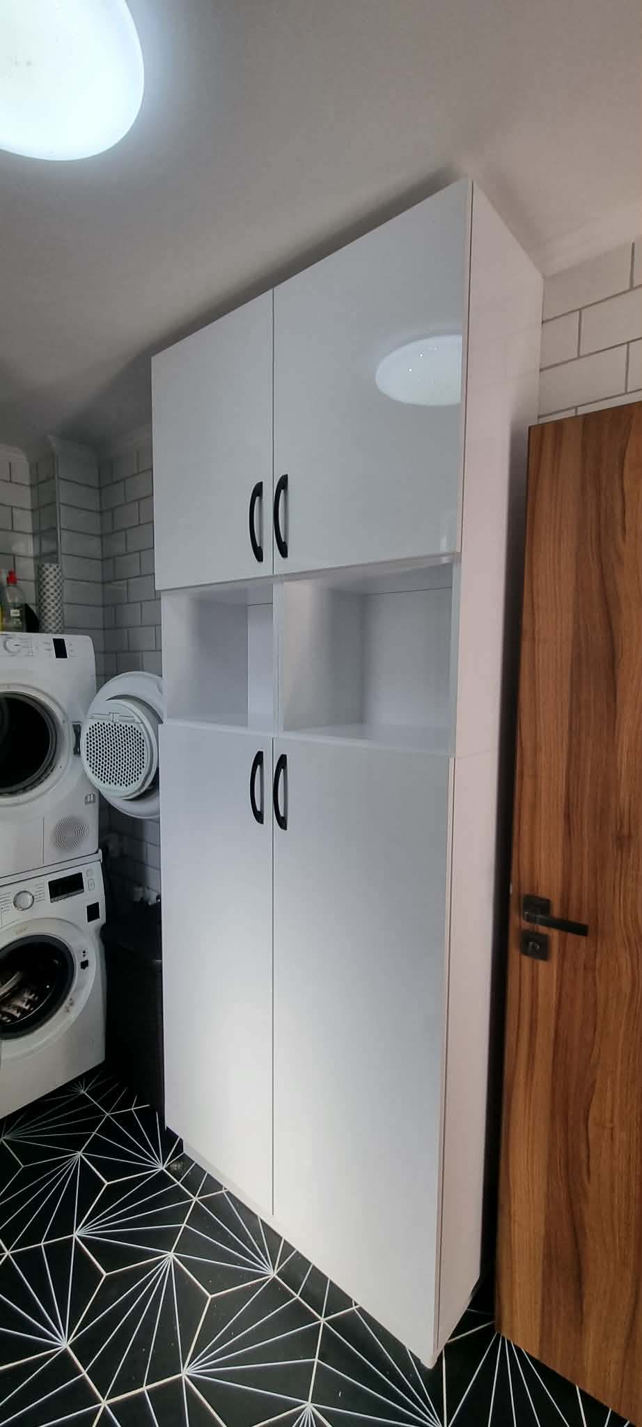 Fényes fehér magas fürdőszobai tárolószekrény fekete fogantyúkkal, nyitott középső polccal